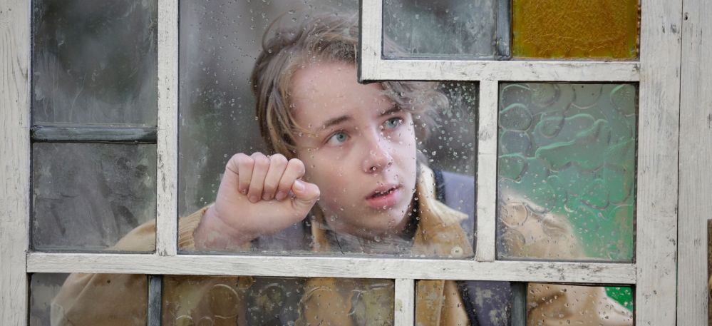 Ein Junge schaut durch eine Fensterscheibe.