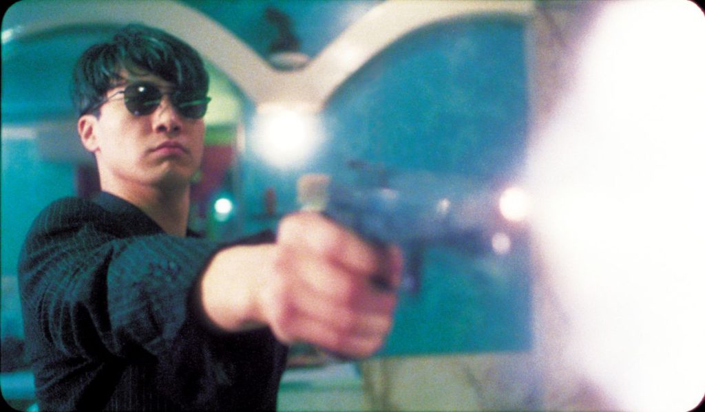 Szenenbild aus Wong Kar-Wais Fallen Angels: Ein Mann mit Sonnenbrille hält eine Pistole und feuert sie ab.