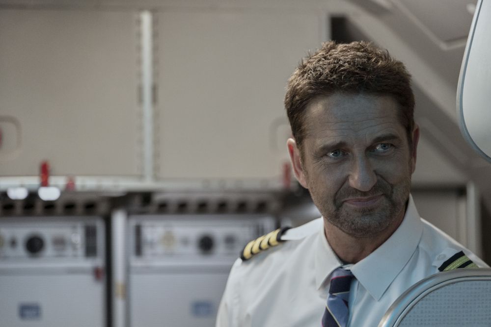 Ein weißer Mittfünfziger in Pilotenuniform an Bord eines Flugzeugs lächelt verhalten.